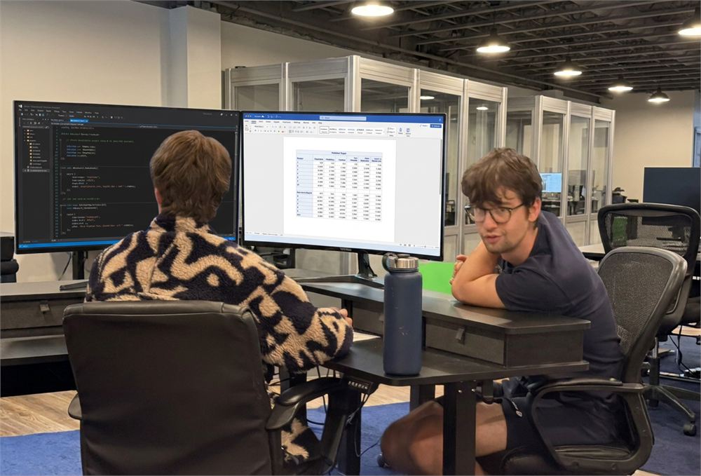 Two Pentara colleagues talking through a problem across the desk, code on the monitors behind them