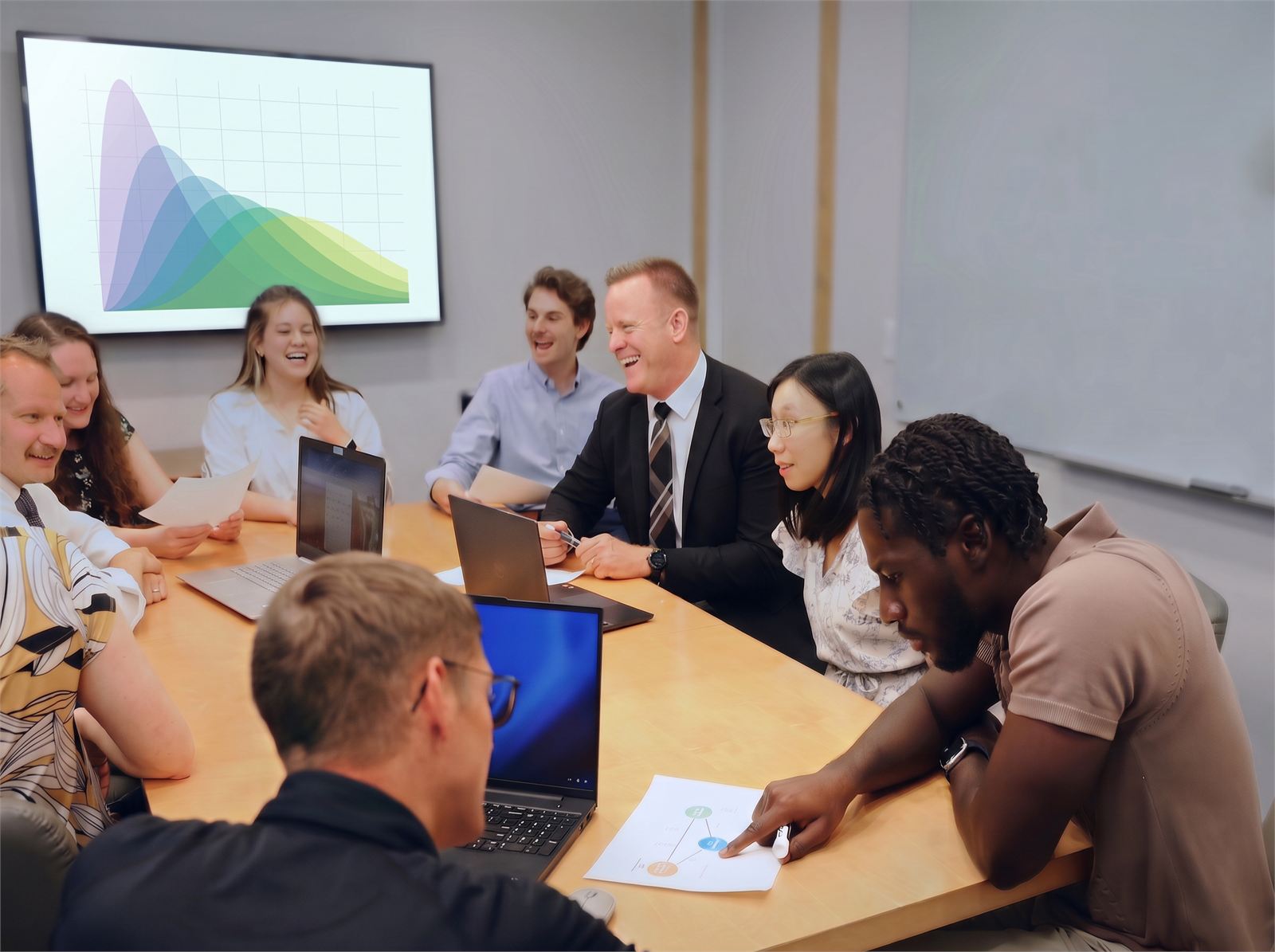 The Pentara team around the conference table mid-discussion, trial data on the wall screen behind them